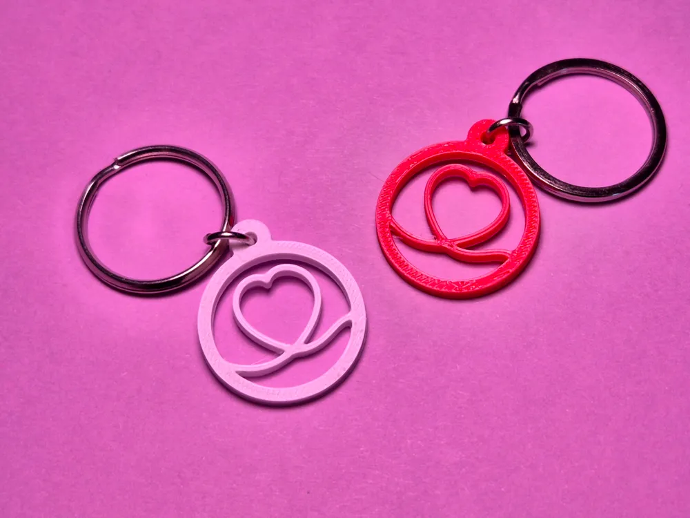 Zwei 3D gedruckte rote Herz-Schlüsselanhänger als Valentinstagsgeschenk auf rosa Hintergrund.